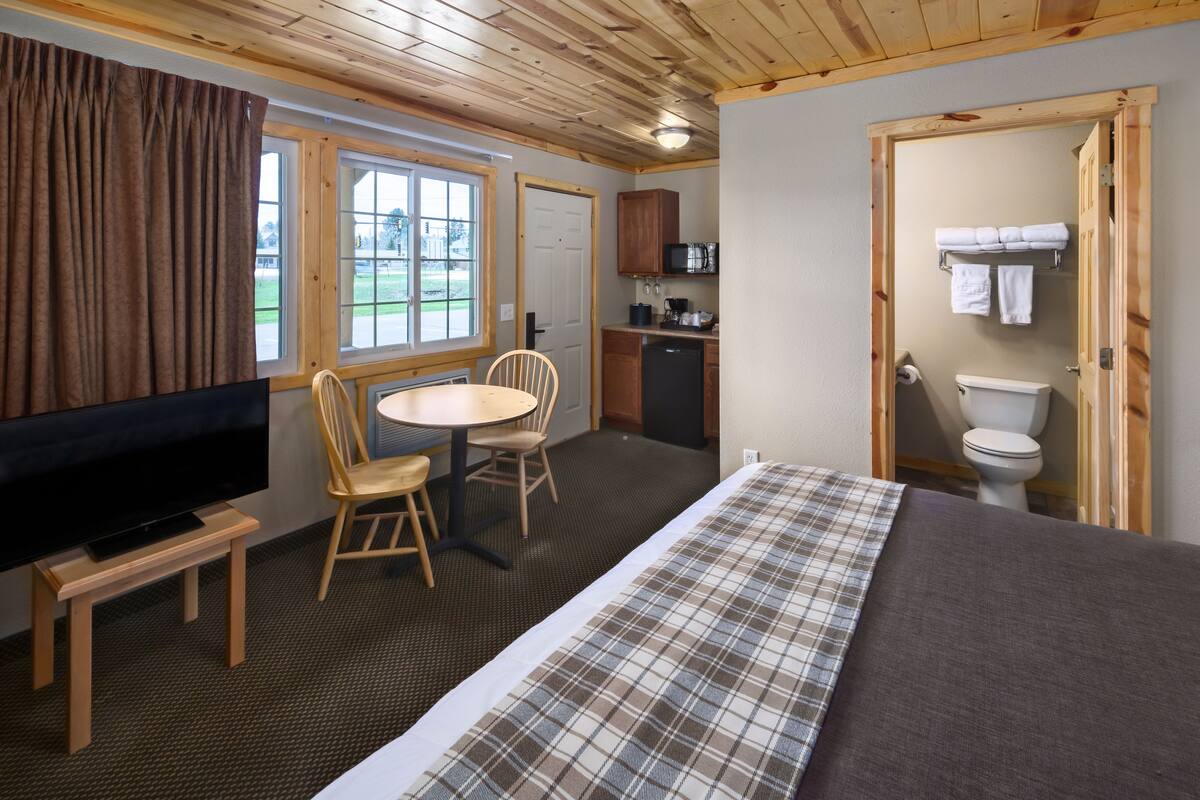 Una stanza con un letto, una televisione, un tavolo da pranzo con sedie, un angolo cottura e un bagno.