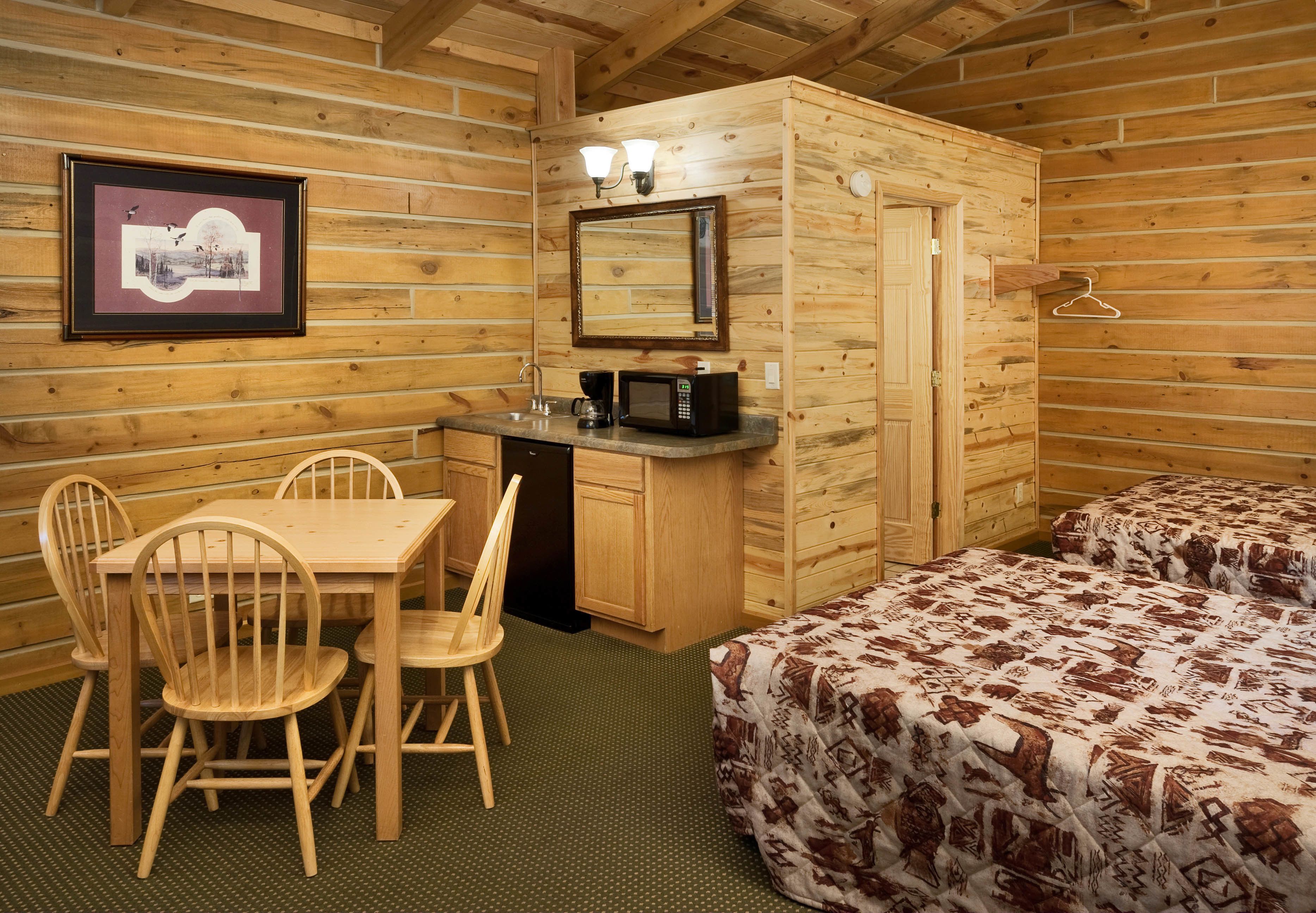 Une pièce de style cabane en bois, avec une table en bois, des chaises, un lit, une petite kitchenette et un tableau encadré au mur.