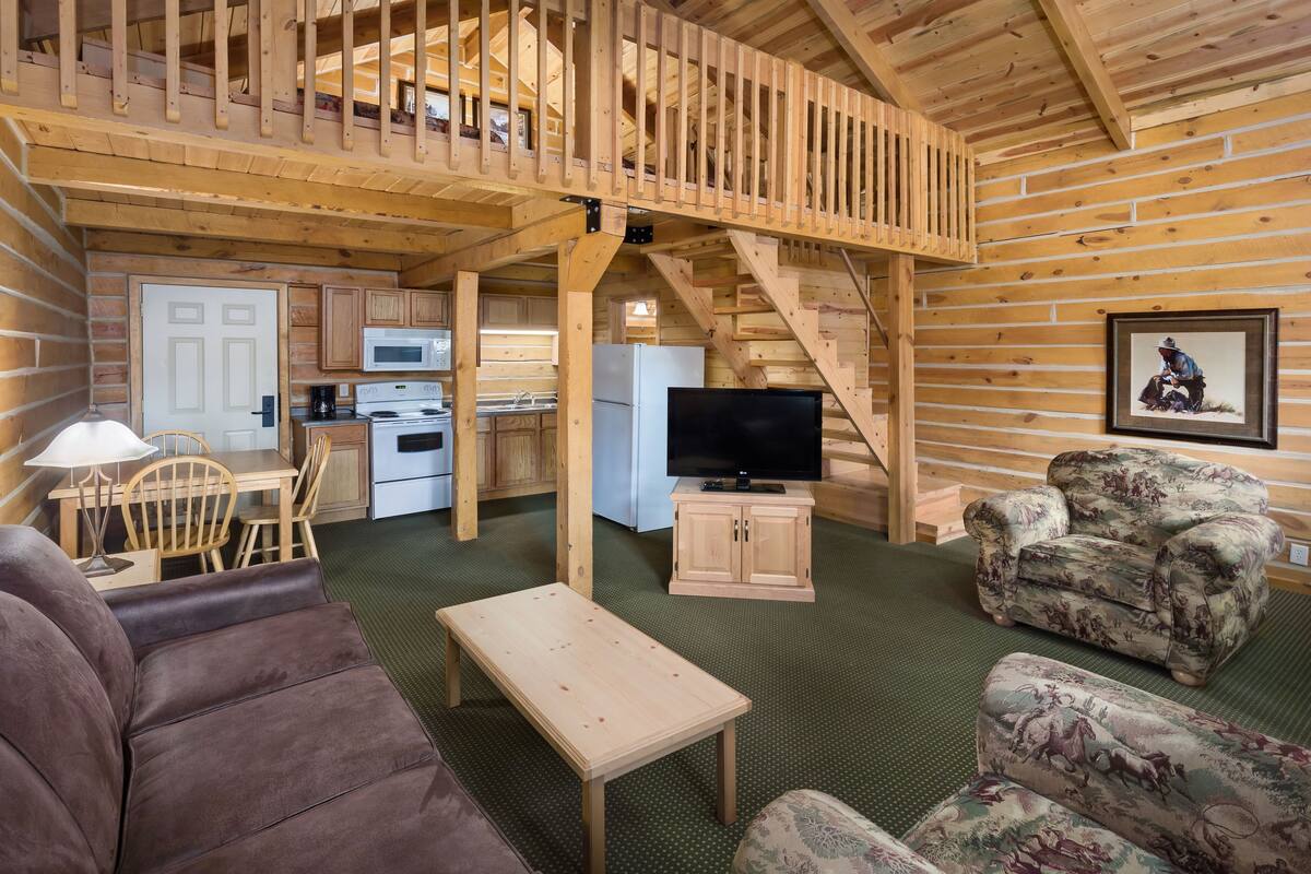 Interno di una baita in legno con zona pranzo, cucina, soggiorno e un balcone.