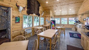 A wooden interior with tables and chairs, a stone fireplace, and large windows. - Rock Crest Lodge And Cabins (Custer)