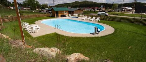Una piscina con sillones de descanso, una terraza de madera y un pequeño edificio al fondo.