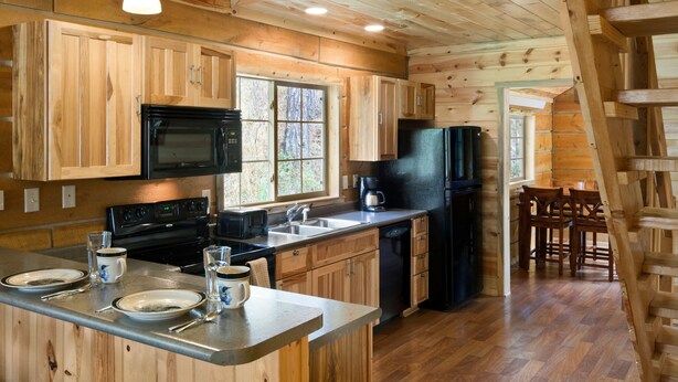 A wooden cabin interior with a kitchen featuring a stove, sink, refrigerator, and wooden cabinets. - Rock Crest Lodge And Cabins (Custer)