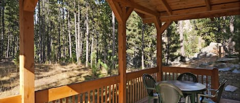 A wooden deck with a table and chairs, overlooking a forested area.