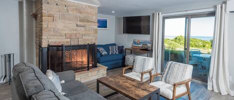 A living room with a stone fireplace, a sofa, a coffee table, and a view of the outdoors.