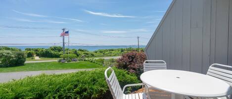 A patio with a table and chairs overlooking a lush green landscape and the ocean.