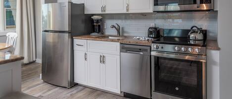 A modern kitchen with stainless steel appliances, white cabinetry, and a granite countertop.