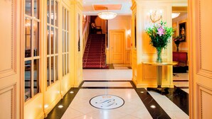 A grand hallway with a marble floor, a chandelier, and a staircase leading to another room.