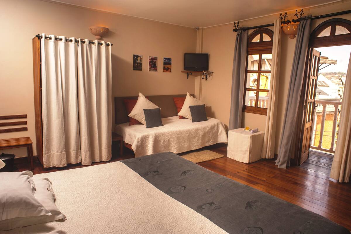 A bedroom with two beds, a TV, and a balcony with curtains.