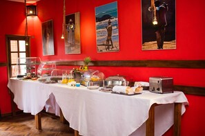 A breakfast buffet with various food items and a toaster, set against a red wall with framed pictures. - Guest House Les 3 Metis (Antananarivo)