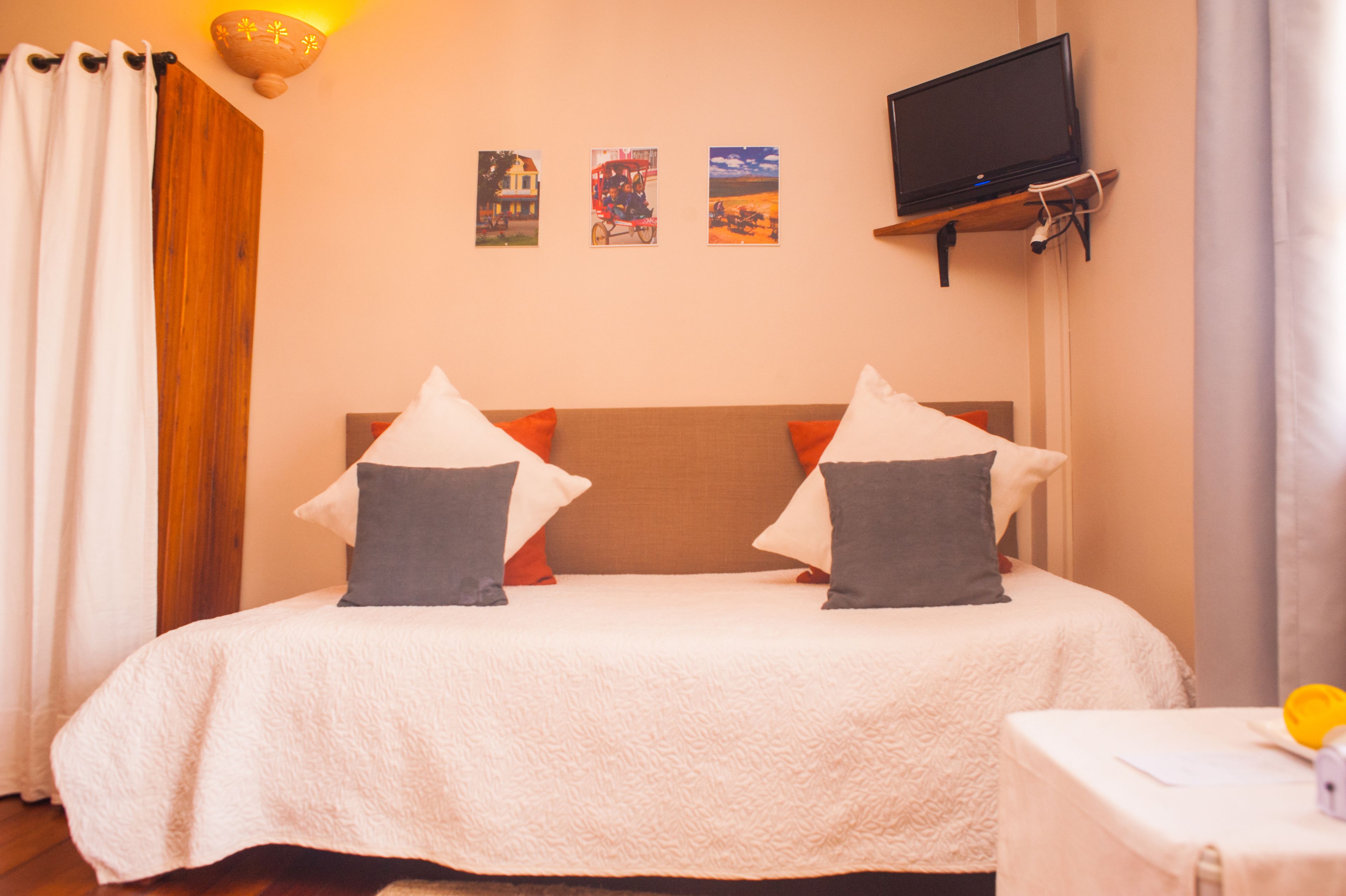 A hotel room with a bed, a television mounted on the wall, and three framed pictures above the bed.