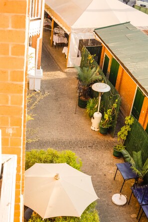 Ein Terrassenbereich im Freien mit Backsteinböden, Blumentöpfen, Sitzgelegenheiten und Sonnenschirmen.