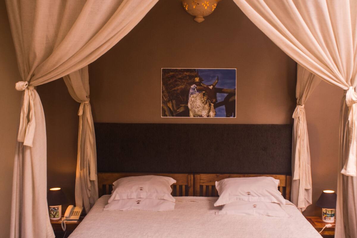A bed with a canopy, a headboard, and a painting on the wall.