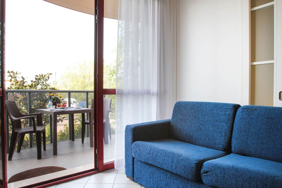 A balcony with a blue sofa, a table with chairs, and a view of greenery outside.