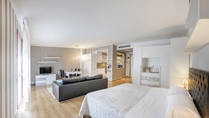 A modern bedroom with a large bed, a sofa, a TV, and a kitchen area in the background. - Residence Venice (Quarto d'Altino)