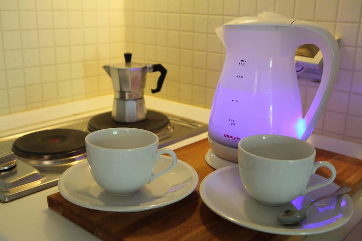 Two white cups on saucers, a coffee maker, and a scale on a wooden board.