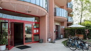 A hotel entrance with glass doors, a reception desk, and a bench with an umbrella. - Residence Venice (Quarto d'Altino)