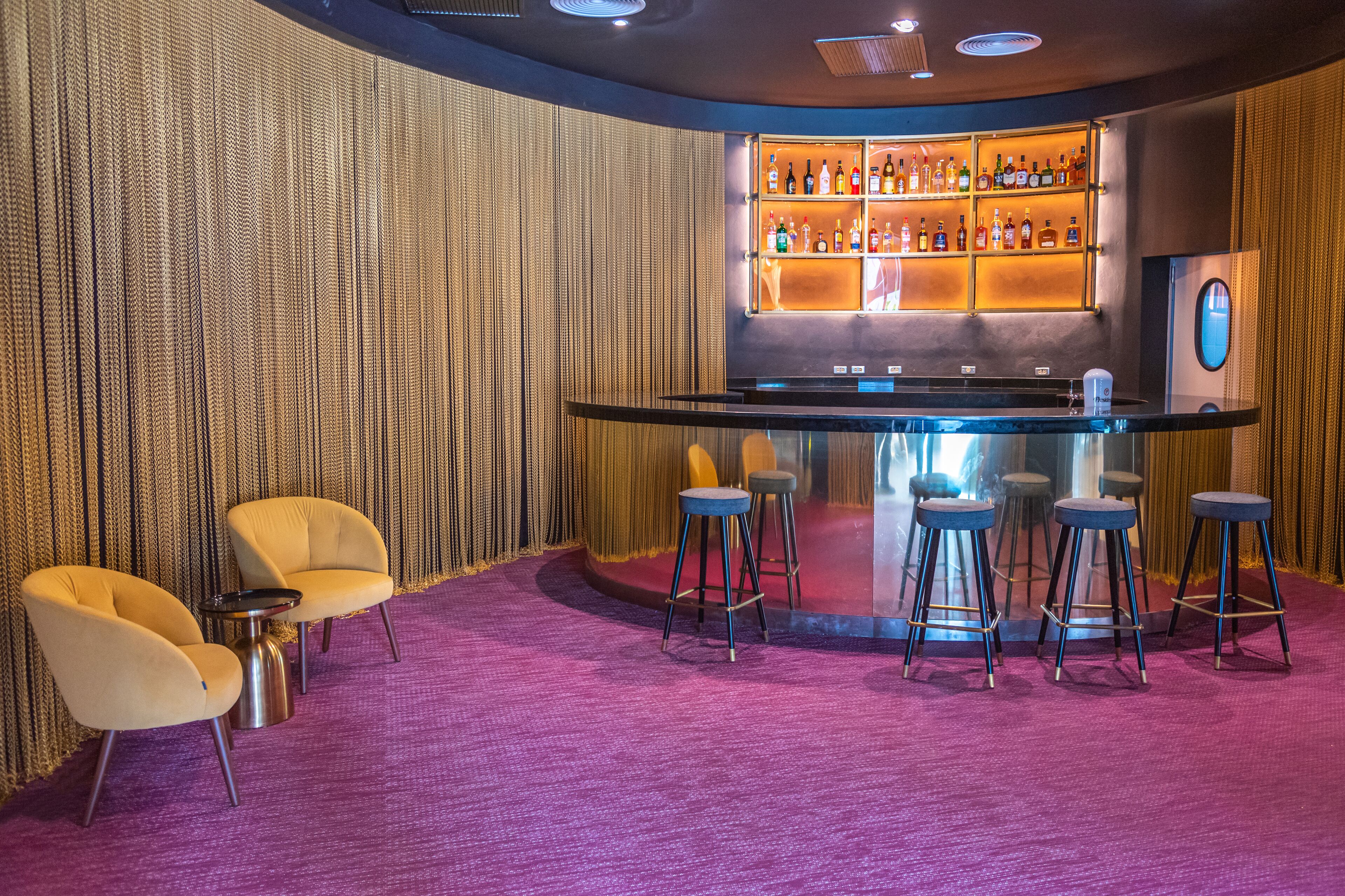 Eine Bar mit Theke, Hockstühlen und einer Flaschenreihe.