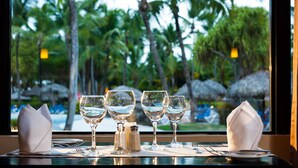 A table set with wine glasses and a salt and pepper shaker, viewed through a window overlooking palm trees and a beach. - Grand Bavaro Princess - All Inclusive (Punta Cana)