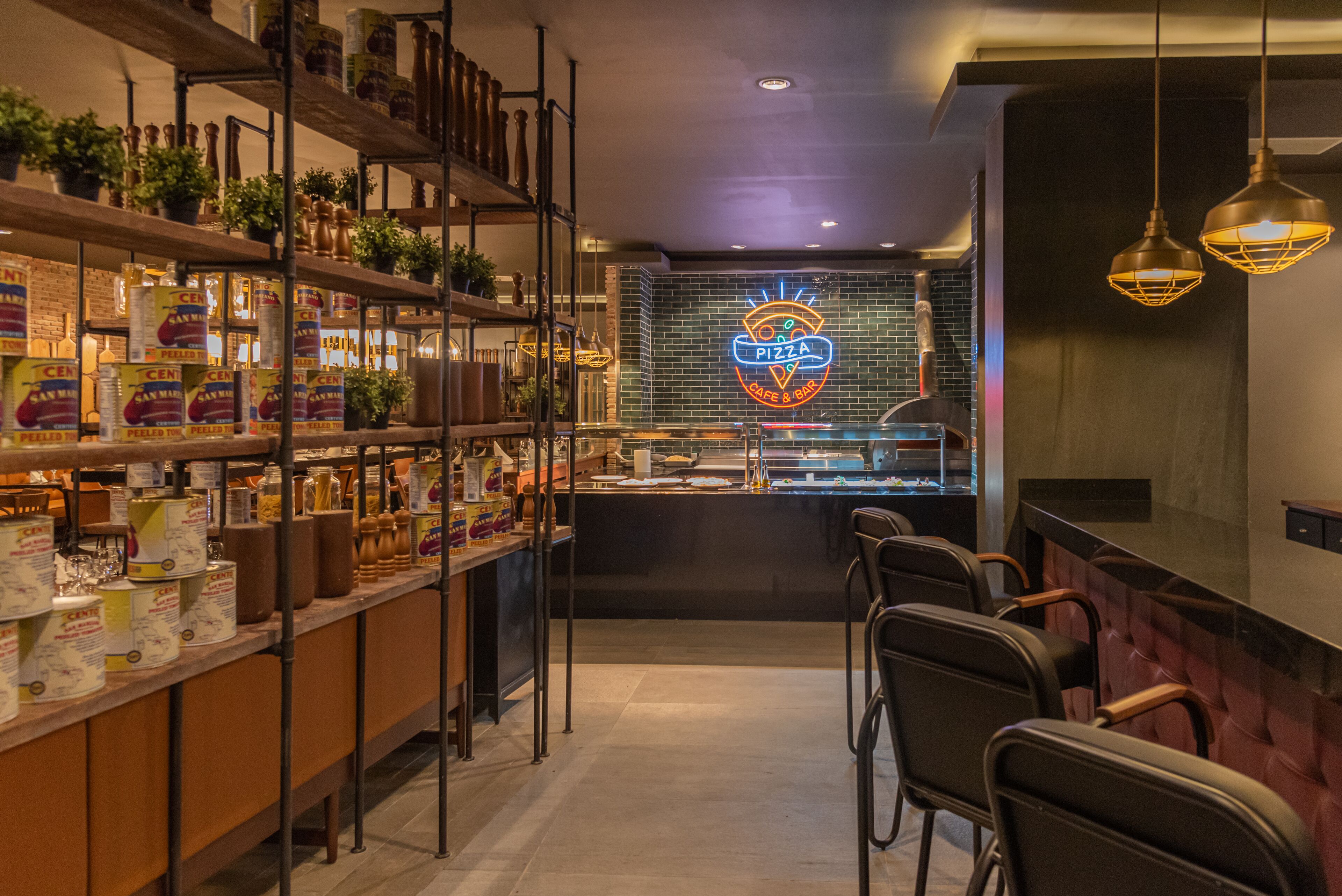 L’intérieur d’un restaurant, avec des étagères remplies de produits alimentaires, un panneau néon représentant une pizza et des sièges au bar.