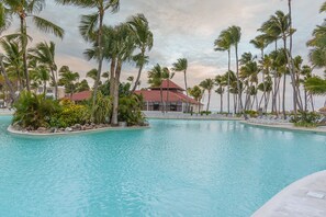 A pool area with palm trees and a building with a red roof.