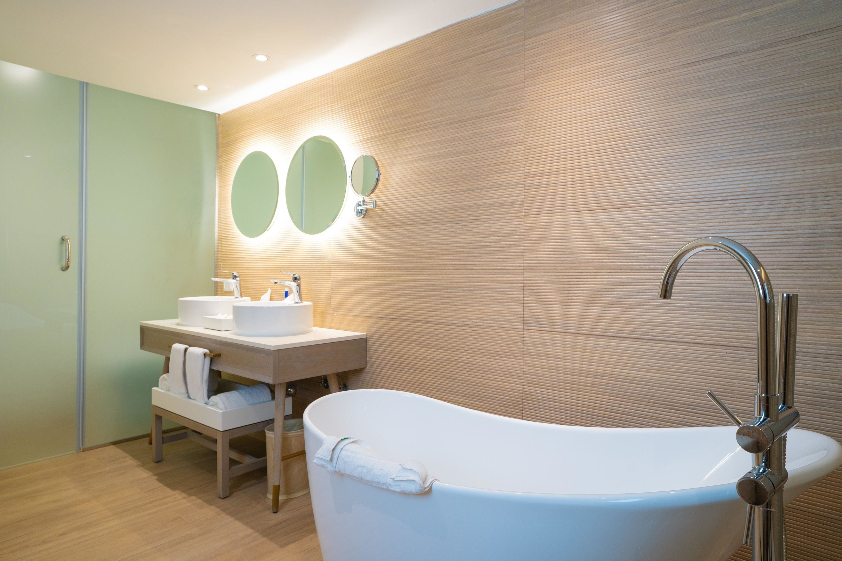 A modern bathroom with a freestanding bathtub, a vanity with a mirror, and a wooden wall panel.