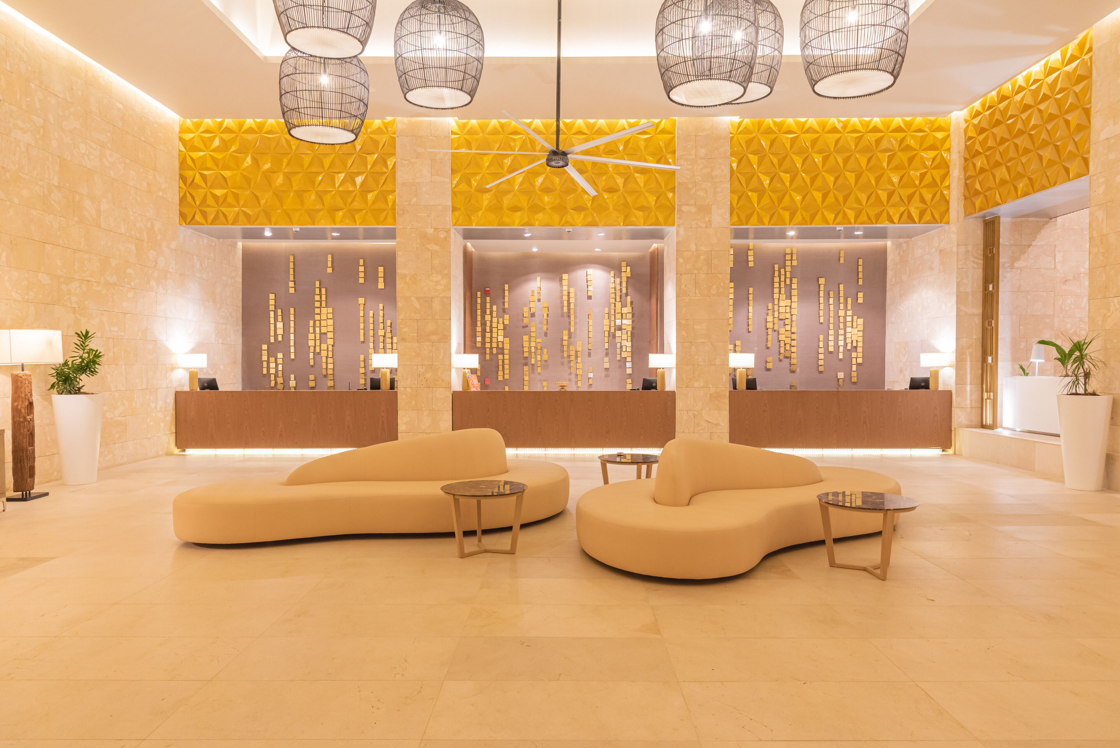 A modern lobby with a reception desk, two sofas, and a ceiling fan.