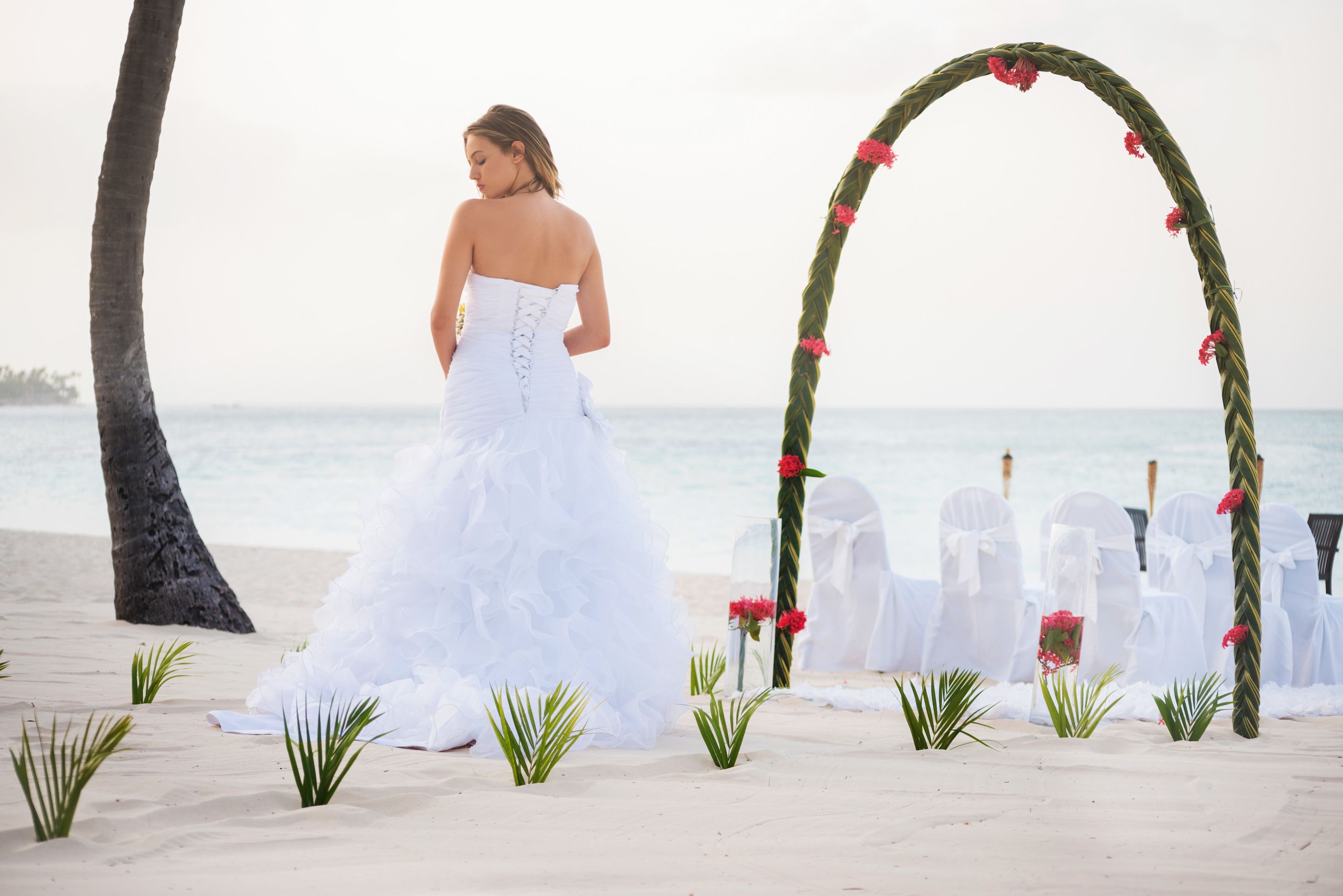 Une cérémonie de mariage organisée sur la plage, avec une arche blanche et des chaises.