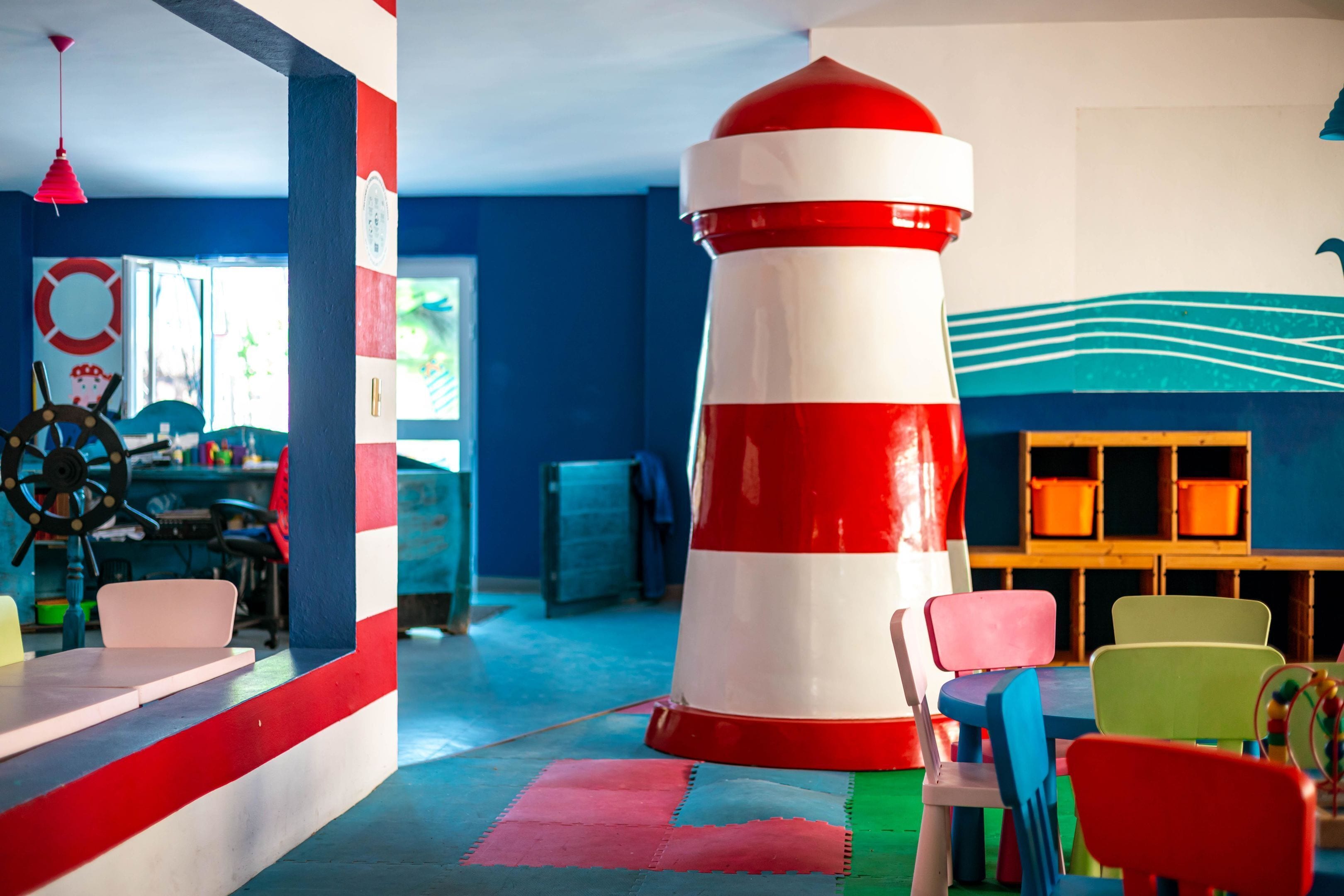 A room with a large red and white lighthouse, colorful chairs, and a table with a life preserver decoration.