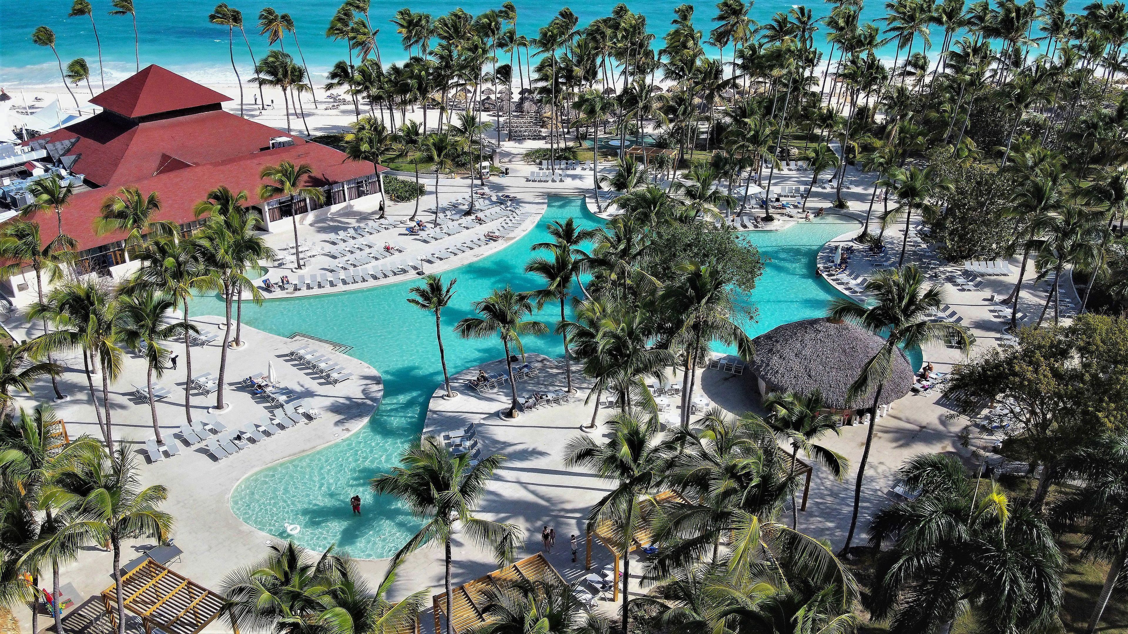 Un resort con piscina central, palmeras y zona de playa.