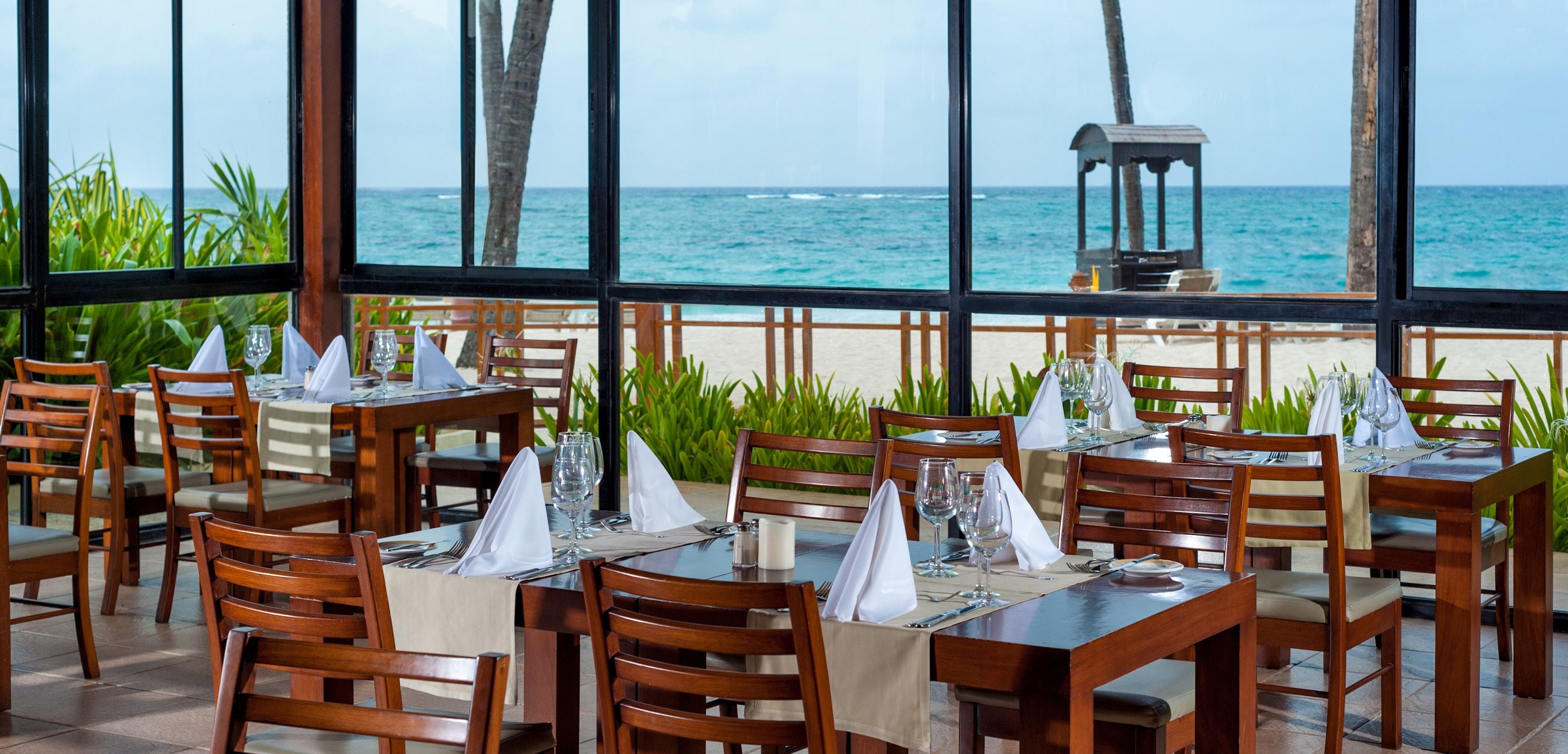 Un restaurant avec des tables et des chaises en bois, situé dans un cadre offrant une vue sur la plage et l’océan.