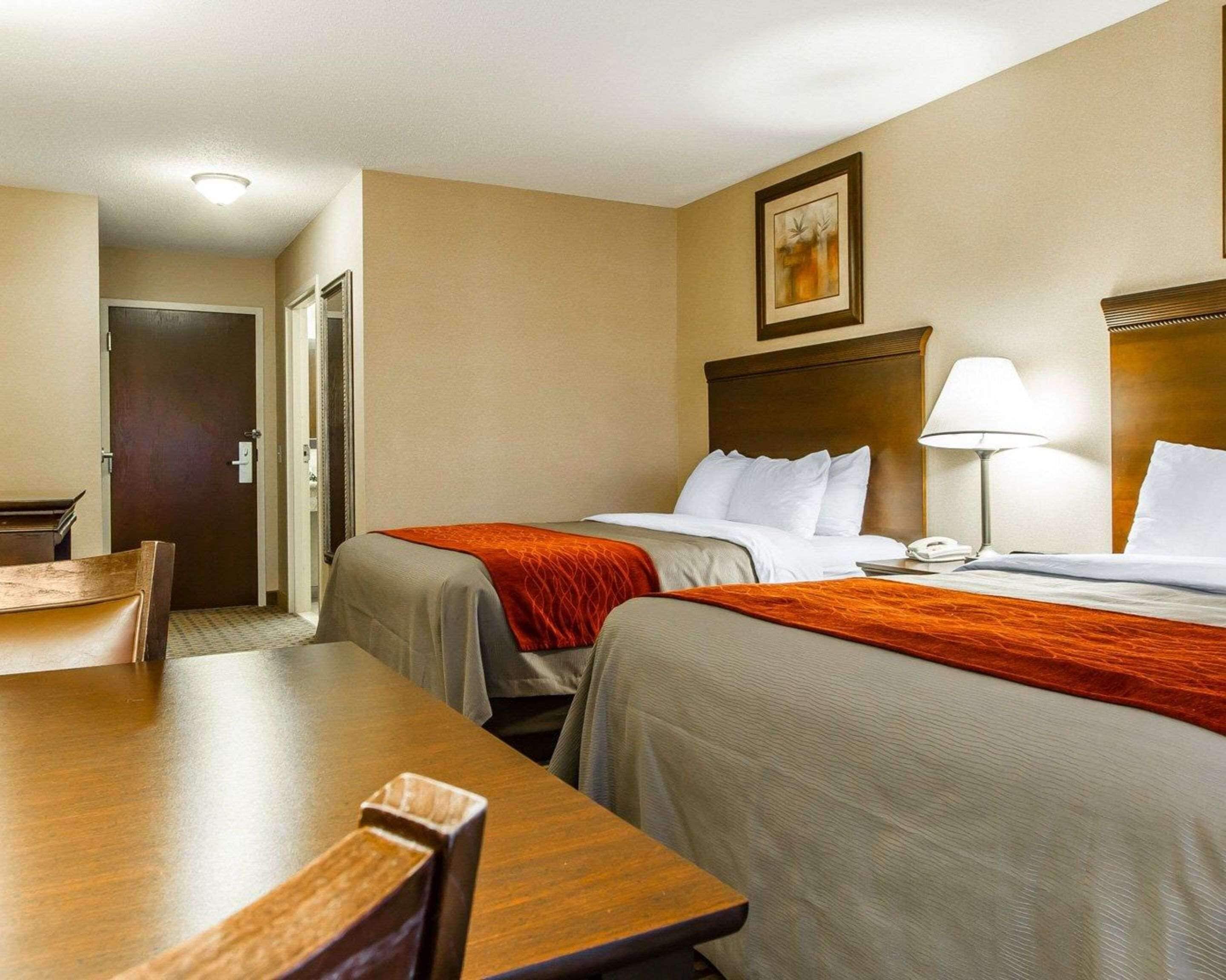 Ett hotellrum med två sängar, ett skrivbord, en stol, en lampa och en tavla på väggen.