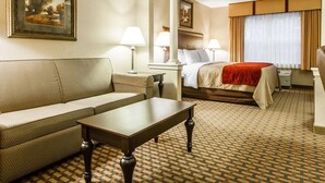 Ein Hotelzimmer mit Sofa, einem Bett mit roter Decke, Schreibtisch und einem gemusterten Teppich.