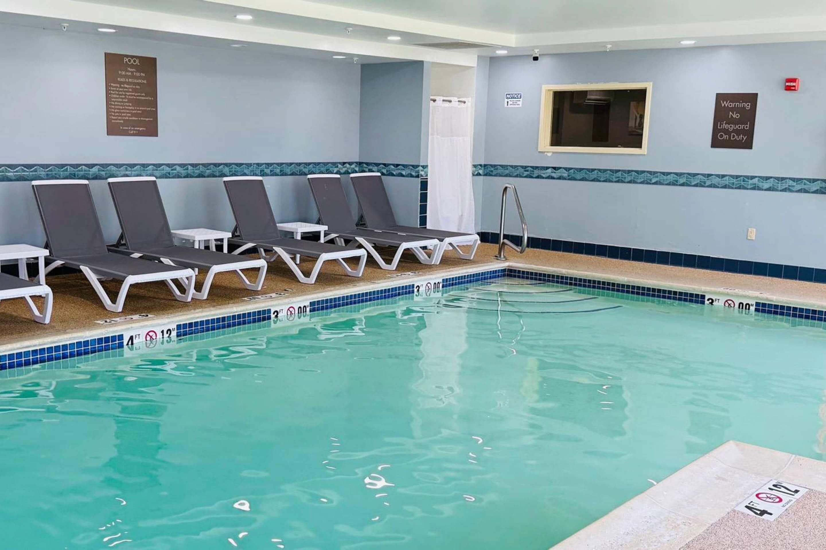 Zona de piscina con sillas de descanso, piscina con agua cristalina y señal de socorrista.