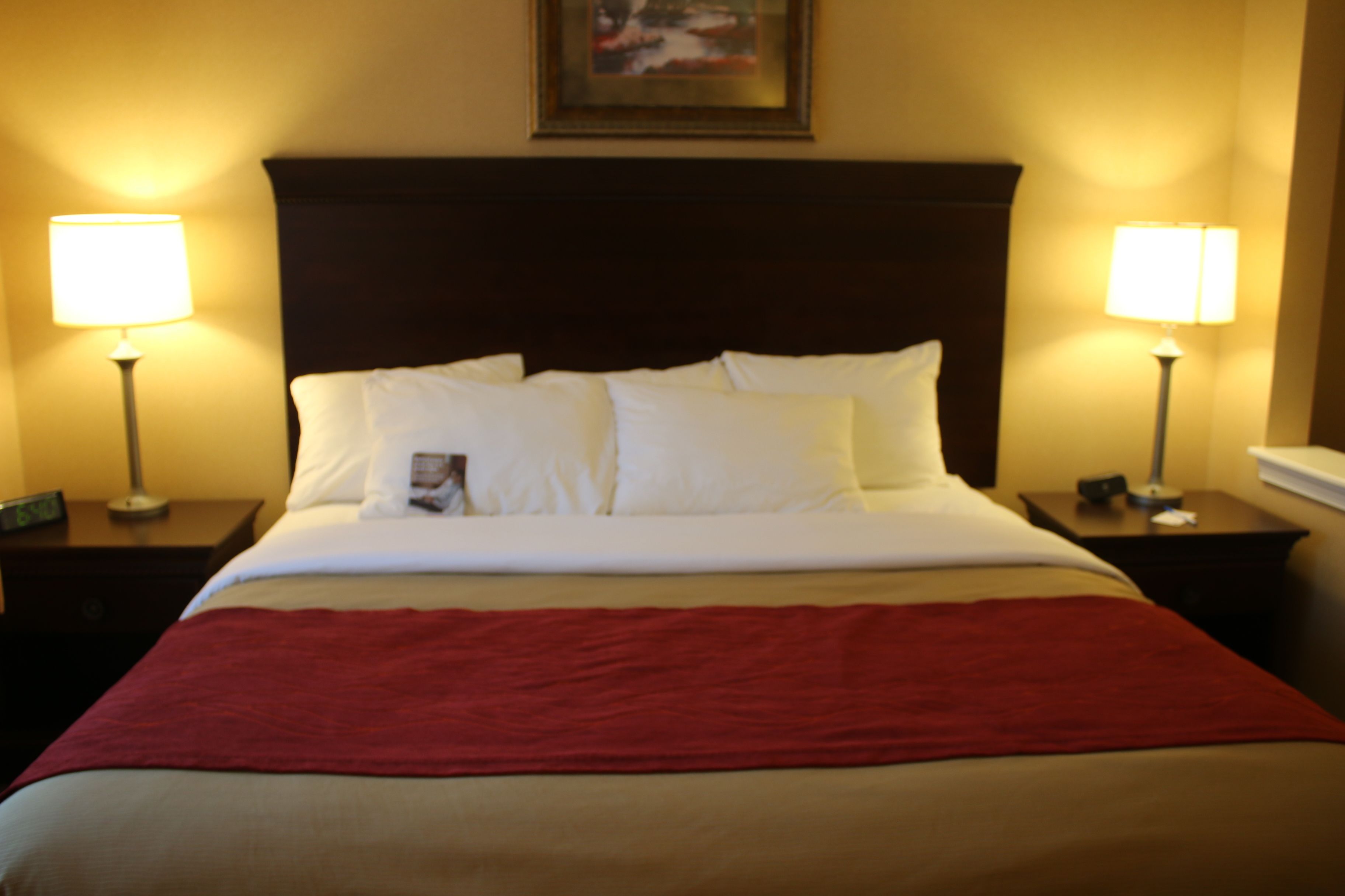 A neatly made bed with white linens and a red blanket, flanked by two bedside tables with lamps.