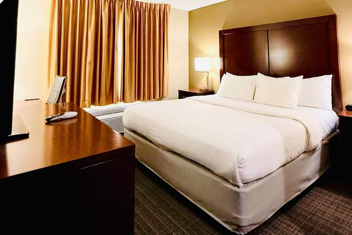 A hotel room with a large bed, a wooden desk, a lamp, and a window with curtains.
