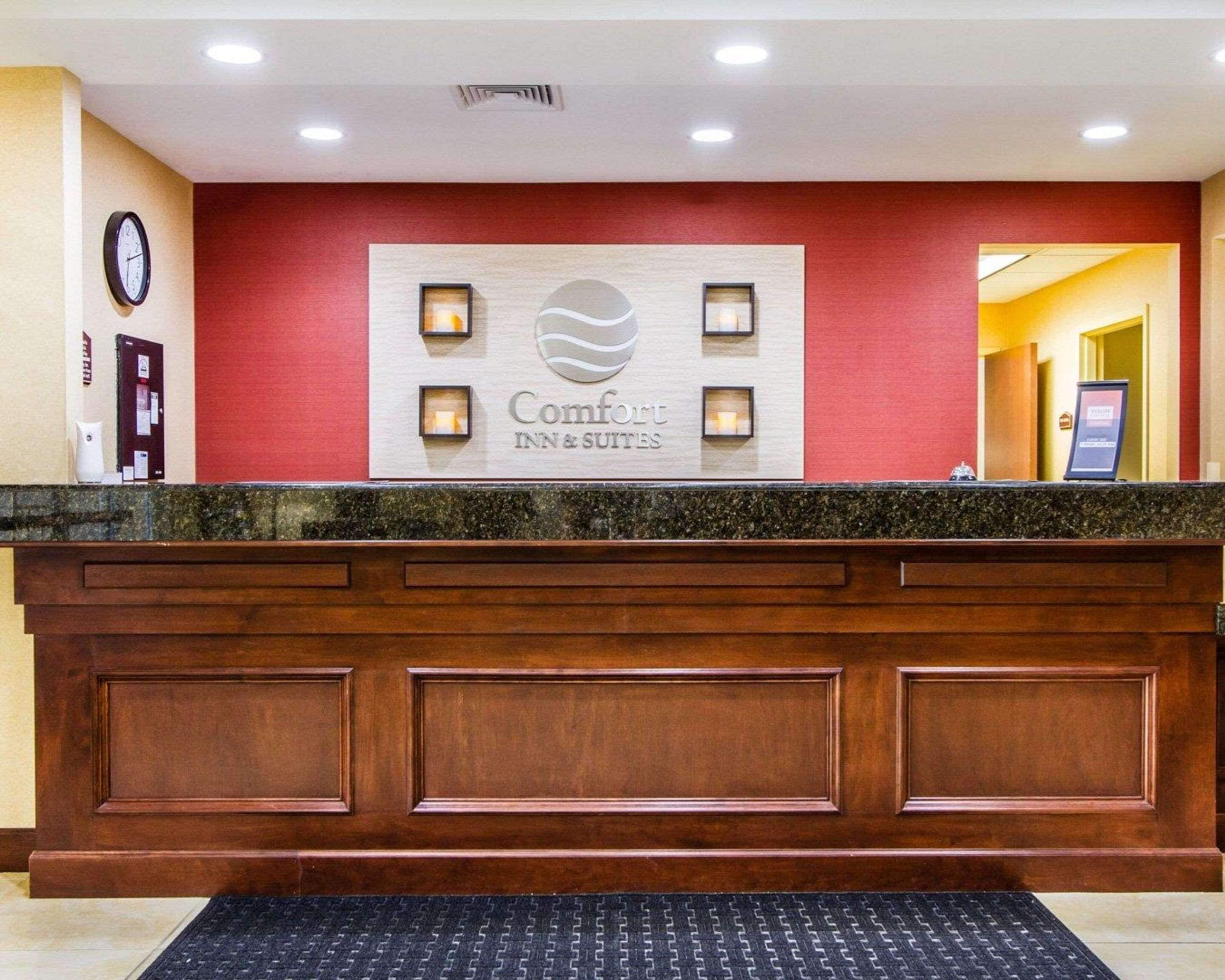 A hotel reception desk with a red wall, a clock, and a sign that reads "Comfort Inn & Suites".