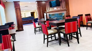 Ein Restaurant mit Holztischen und -stühlen, einem an der Wand befestigten Fernseher und einer Theke im Hintergrund.