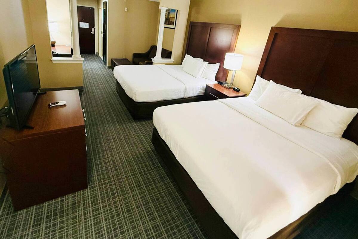 A hotel room with two beds, a TV, a desk, and a mirror.
