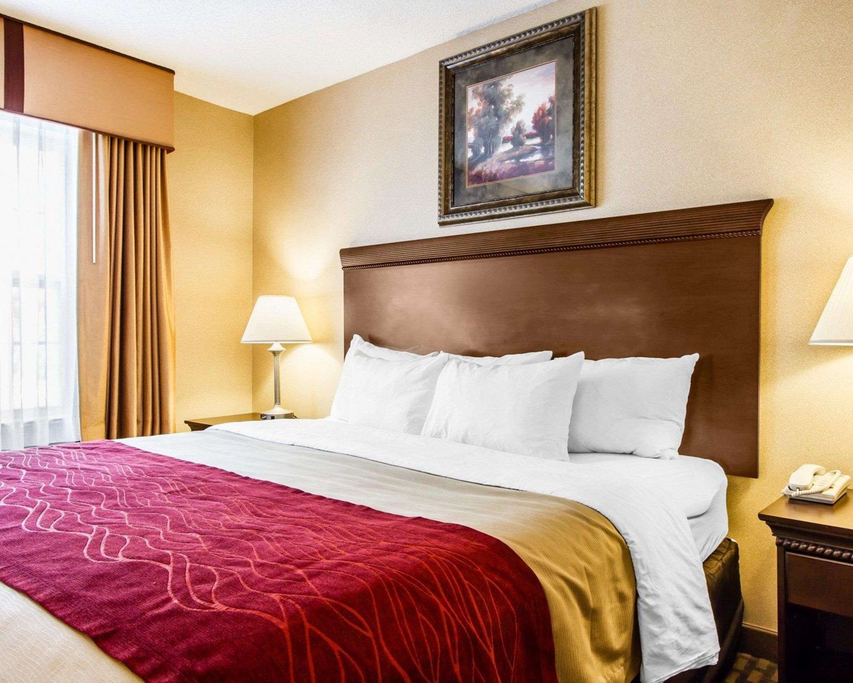 A hotel room with a large bed, a red and gold bedspread, two bedside lamps, a framed picture on the wall, and a telephone on a nightstand.