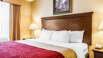 A hotel room with a large bed, a red and gold bedspread, two bedside lamps, a framed picture on the wall, and a telephone on a nightstand.