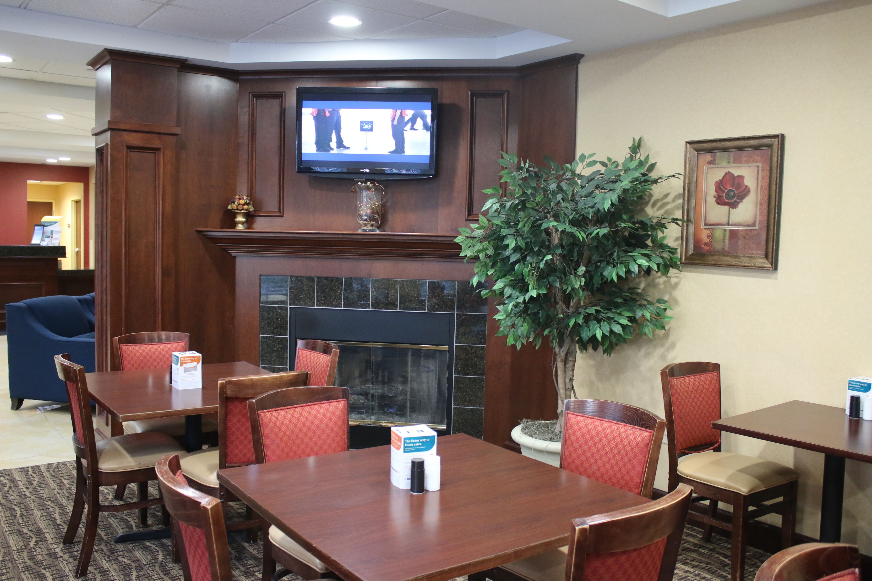 A hotel lobby with a fireplace, a television mounted above it, and several tables and chairs.