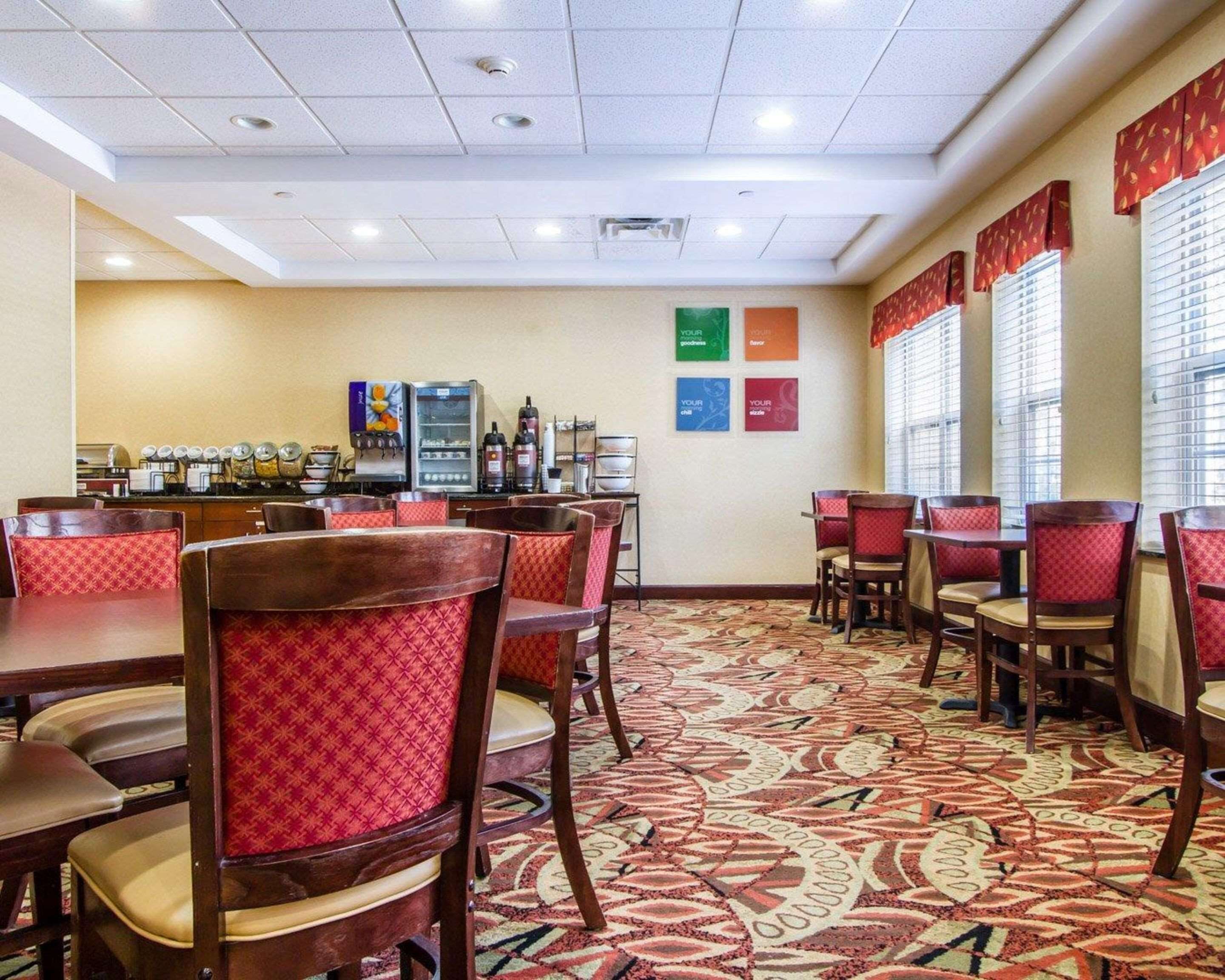 A hotel dining area with multiple tables and chairs, a coffee machine, and a wall with motivational posters.