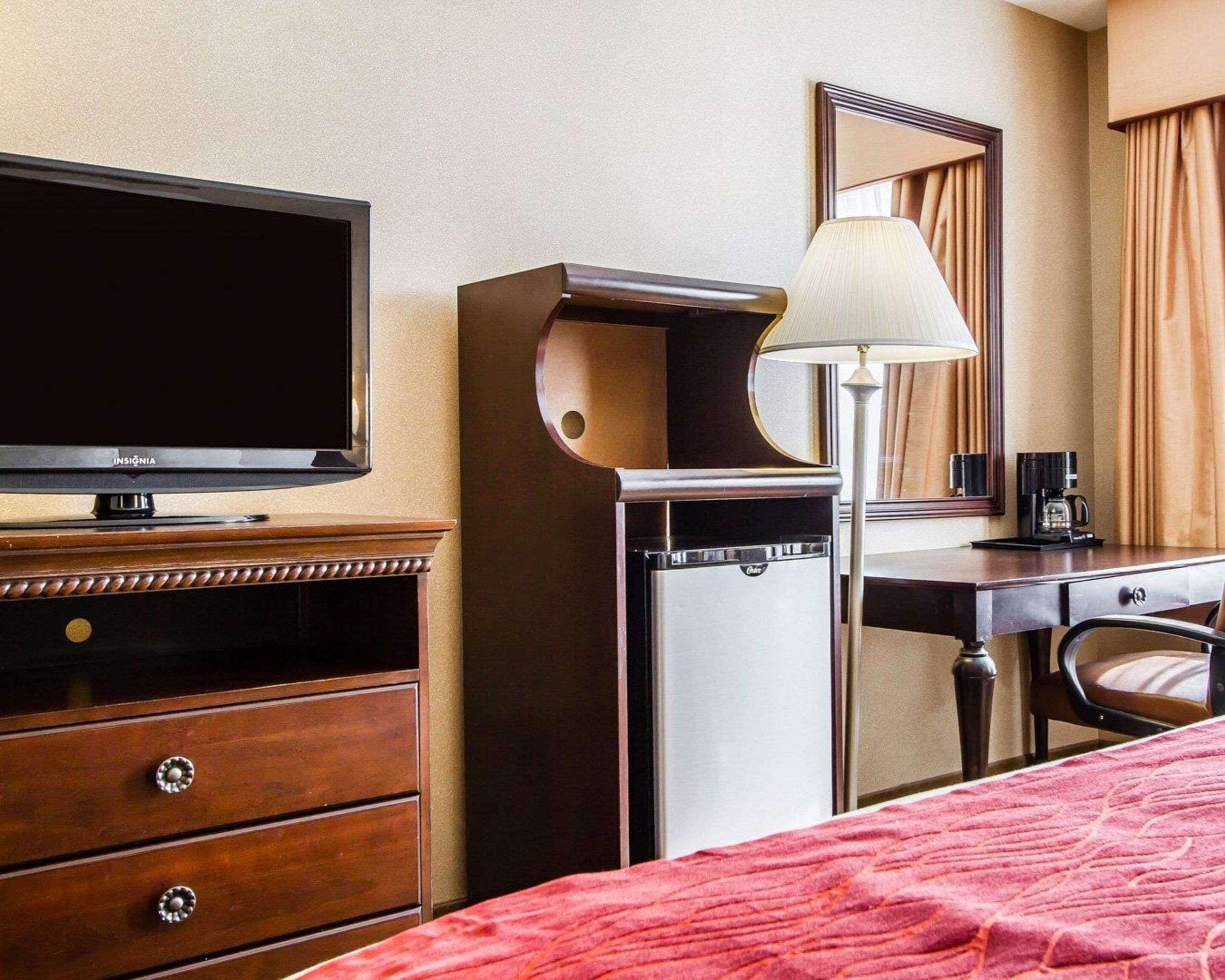 A hotel room with a bed, a TV, a desk with a lamp, a coffee maker, and a dresser.