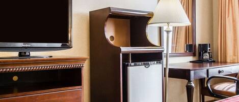 A hotel room with a bed, a TV, a desk with a lamp, a coffee maker, and a dresser.