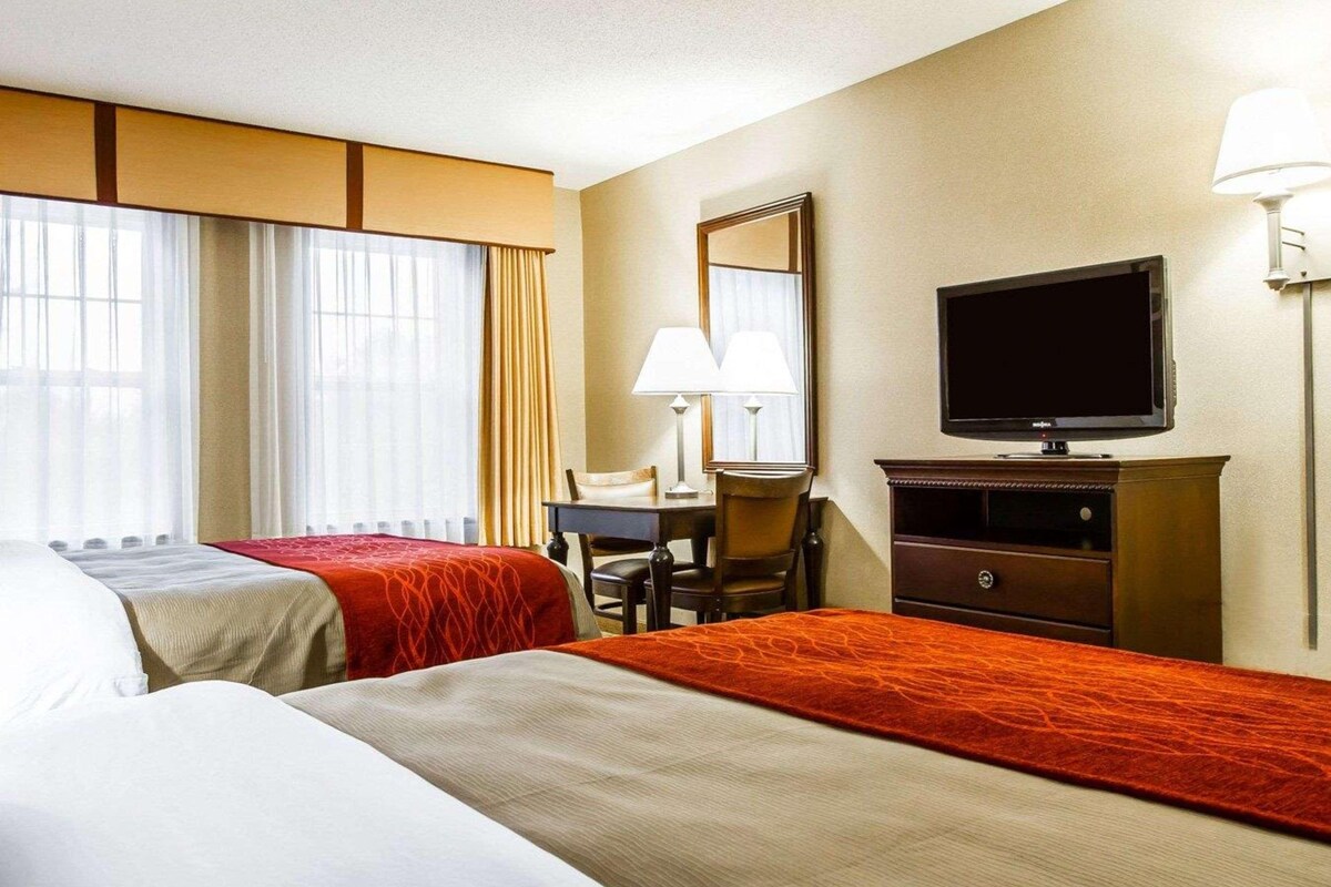 Une chambre d’hôtel avec deux lits, un bureau, une chaise, une télévision et une lampe.