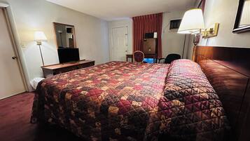 A hotel room with a large bed, a desk with a chair, a television, and a mirror.