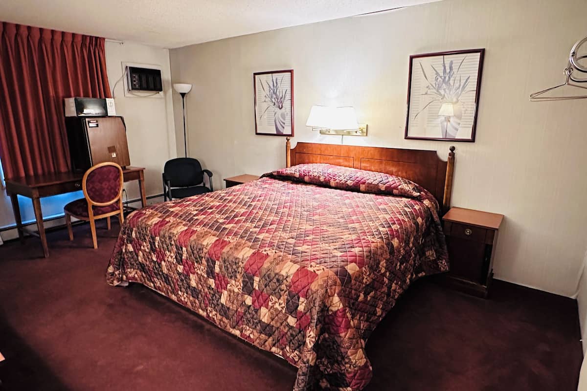 A hotel room with a large bed, a desk with a chair, a TV, and two framed pictures on the wall.