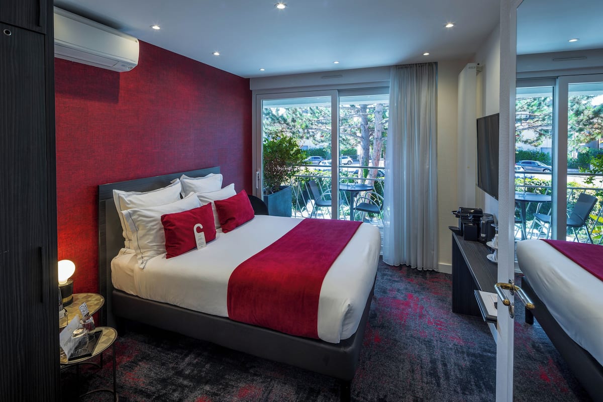 A hotel room with a large bed, a desk, a TV, and a balcony with a view of the outside.
