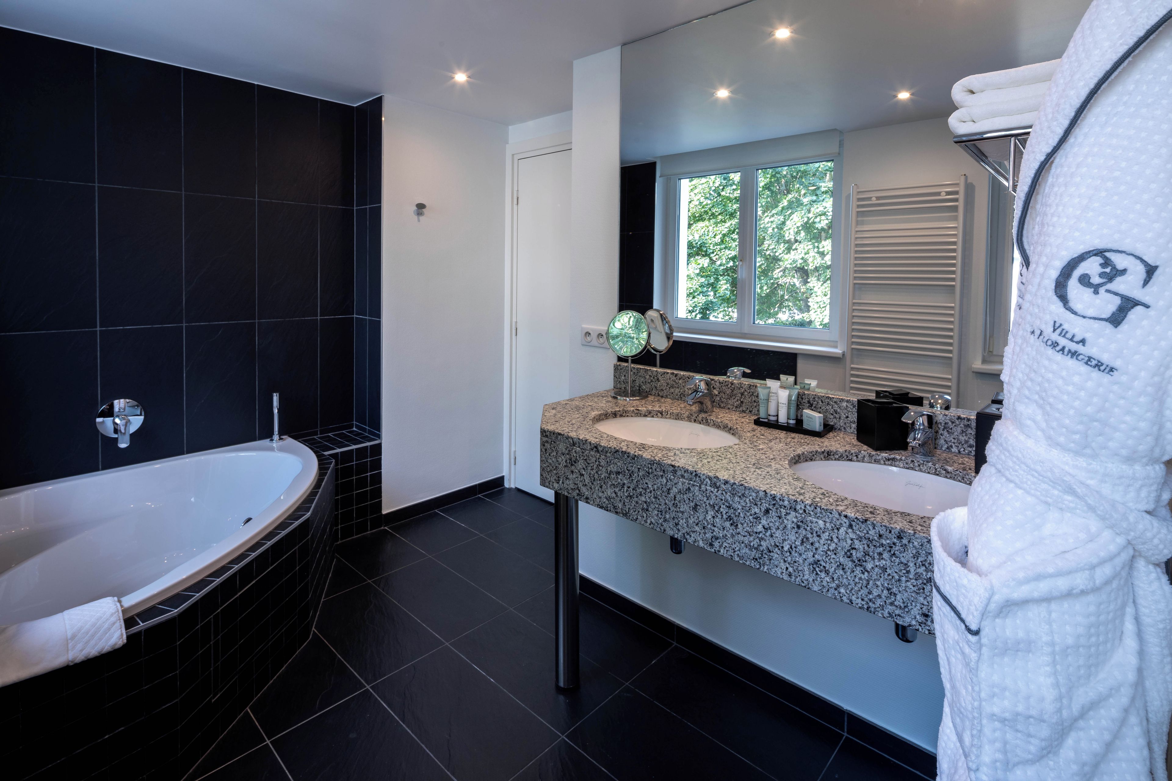 Ein modernes Badezimmer mit einer freistehenden Badewanne, zwei Waschbecken mit Granitablagen und einem großen Spiegel.
