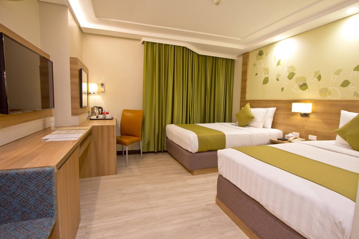 Ein Hotelzimmer mit zwei Betten, einem Schreibtisch, einem Stuhl, einem Fernseher und einem grünen Vorhang.